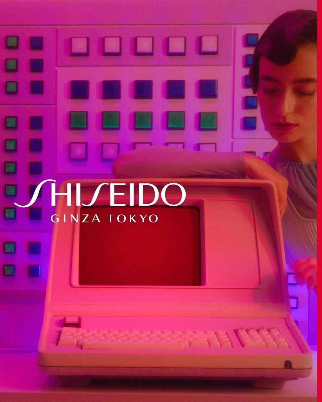 Beauty shot featuring a woman in stylish top next to an old computer and a wall of buttons, bathed in neon pink light. Shiseido logo visible.