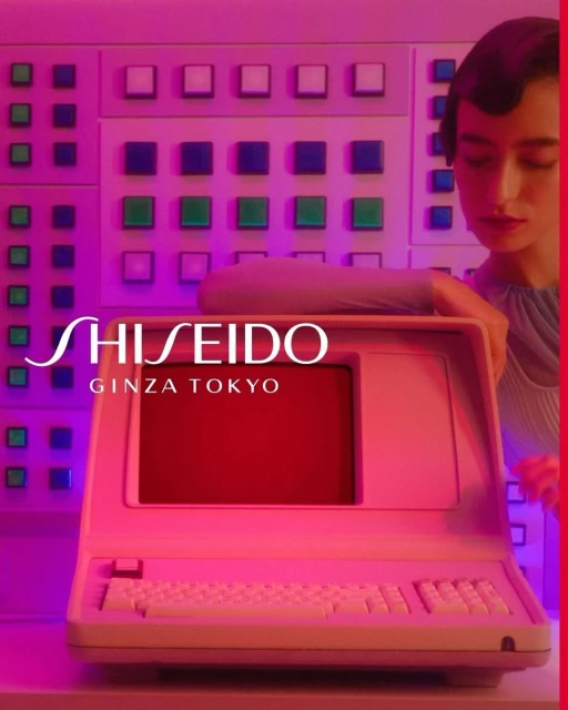 Beauty shot featuring a woman in stylish top next to an old computer and a wall of buttons, bathed in neon pink light. Shiseido logo visible.