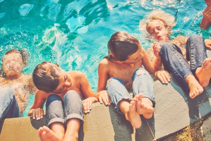 Children sitting on the edge of a swimming pool with legs dangling in bright turquoise water