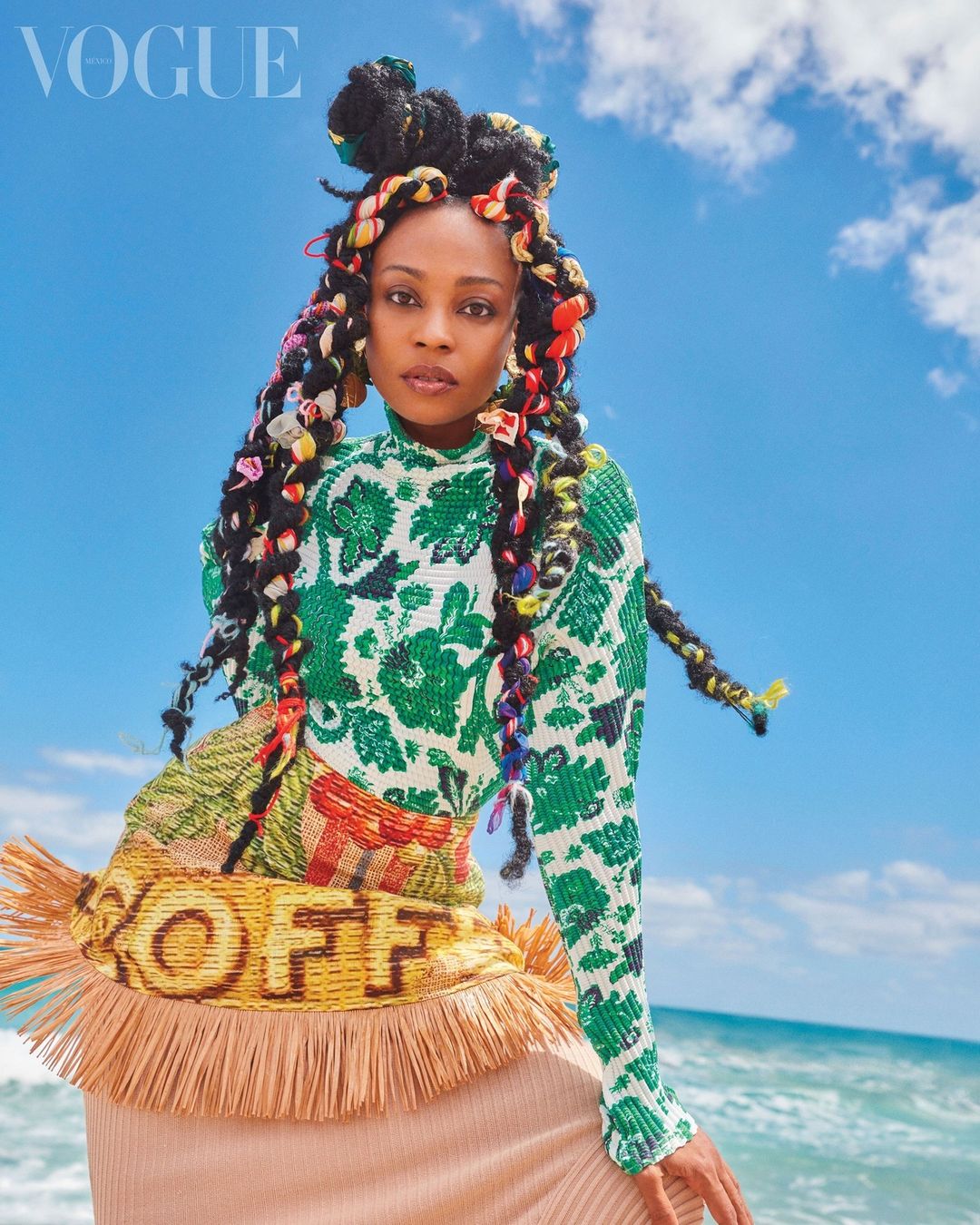 Portrait of a Black woman with braids and a patterned top against a sky and beach background for a fashion editorial in Vogue.