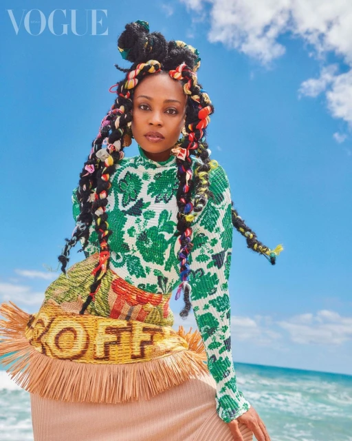 Portrait of a Black woman with braids and a patterned top against a sky and beach background for a fashion editorial in Vogue.