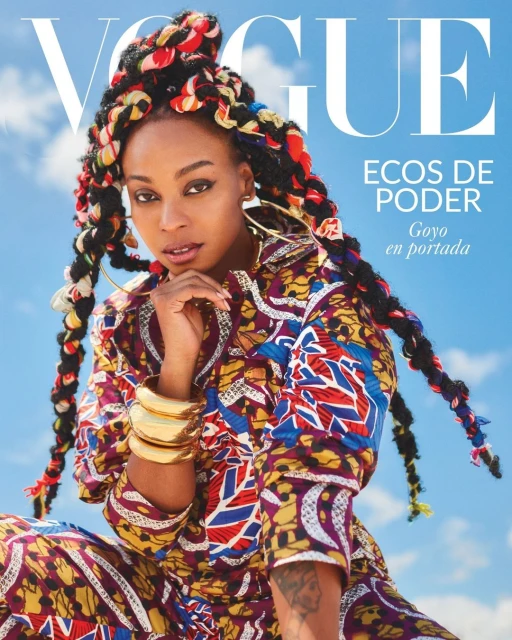 Fashion magazine cover featuring a woman with colorful braids wearing a patterned outfit against a bright blue sky backdrop.