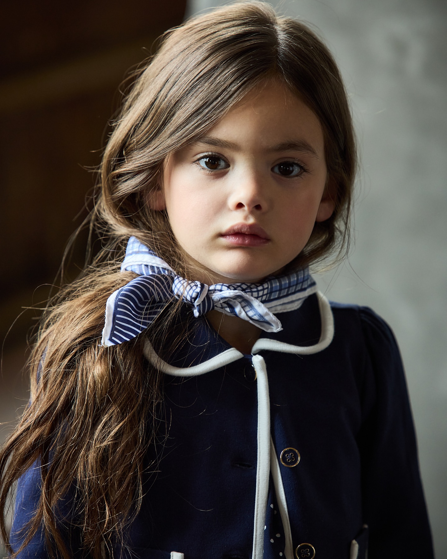 Close-up portrait of a child wearing a dark blue jacket with white piping and a blue-and-white patterned neck scarf.