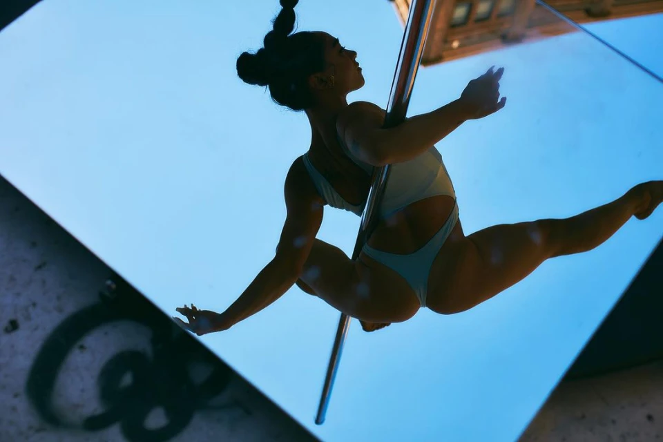 Adult female pole dancing outdoors in pale aqua bodysuit. Shot of acrobat in urban setting doing acrobatic performance.