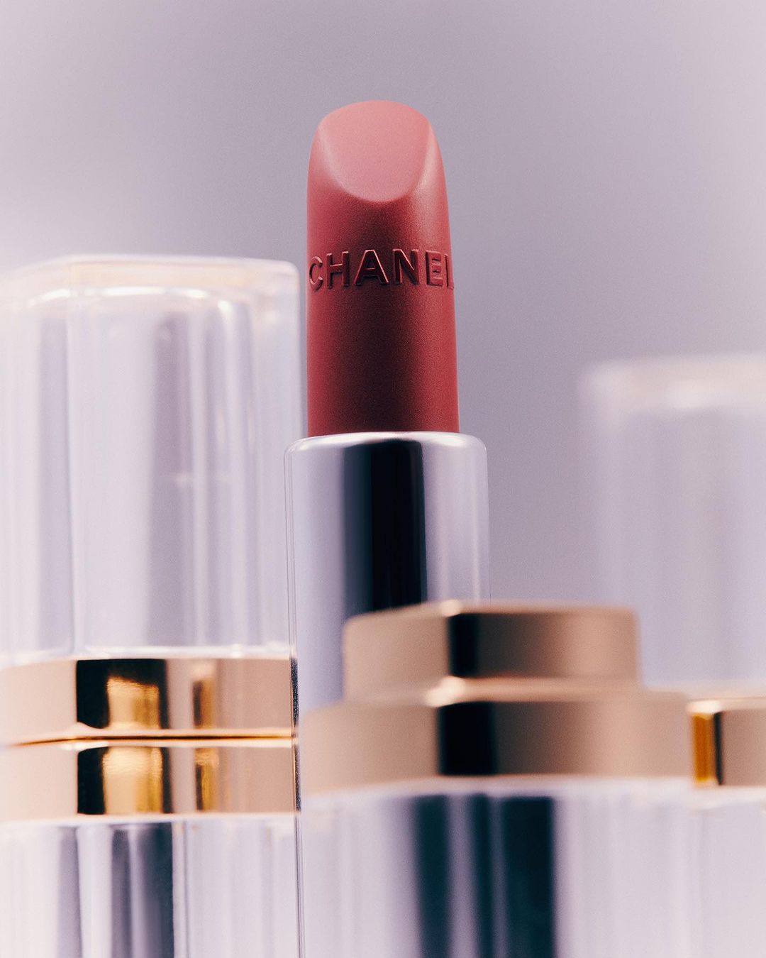 Close-up of a rose-colored Chanel lipstick with a clear and gold tube. The lipstick tube has the brand name vertically printed on it.