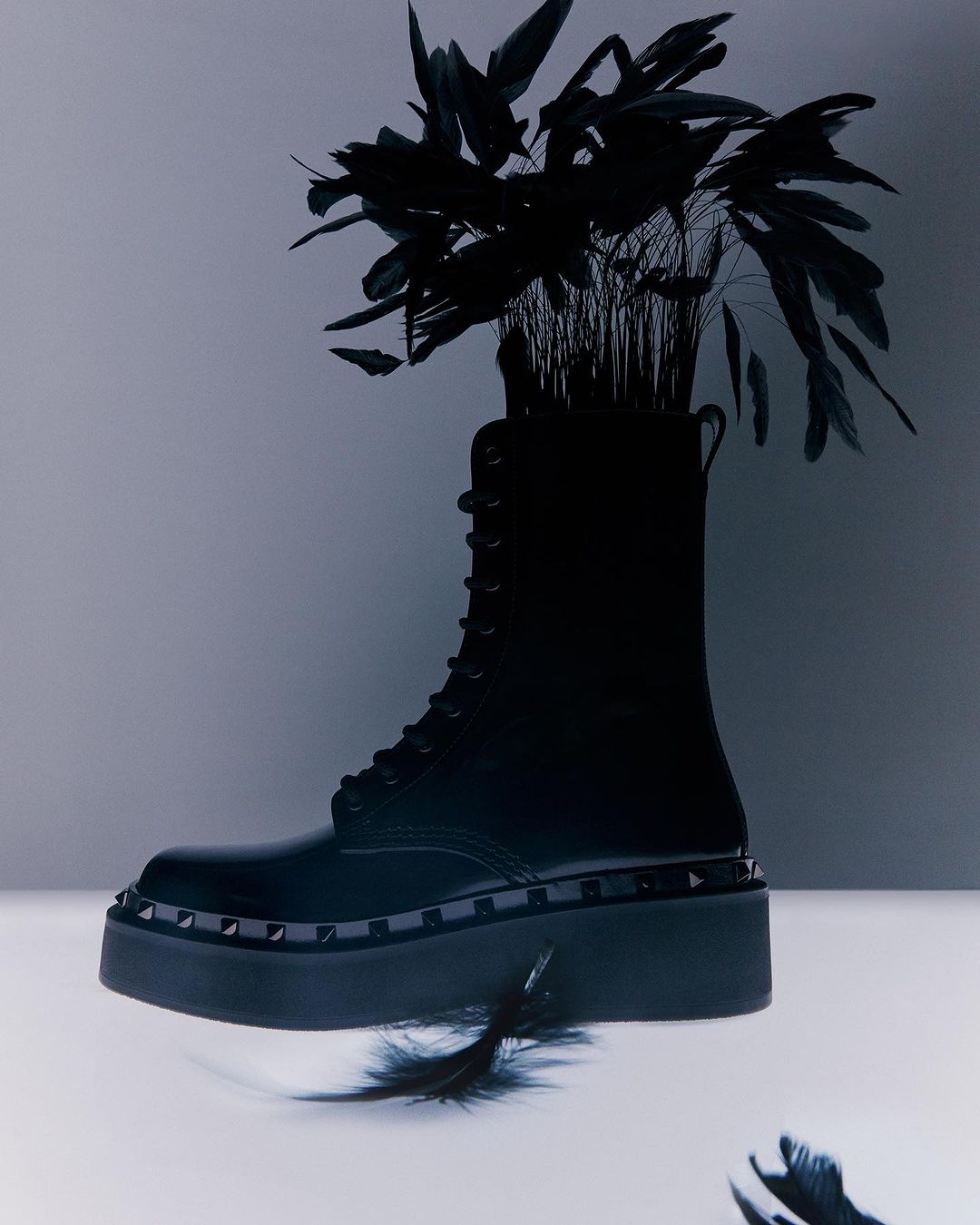 Studio shot of a black platform boot with laces filled with black feathers, isolated on a gradient grey and white background.