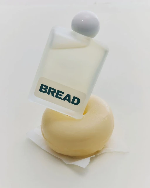 Still life of a frosted glass bottle with the word 'BREAD' displayed on it resting on a white donut and paper towel against a white background.