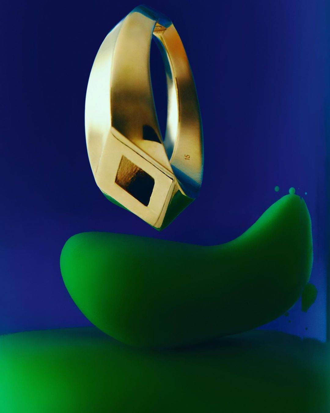 Golden ring on green abstract podium against blue backdrop. Jewellery product shot highlights smooth textures, angular shapes, and solid colors.