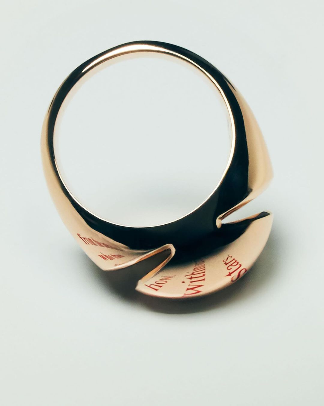 Close-up of a rose gold ring with engraved text against a white background. Jewelry design featuring a unique band. Studio lighting.