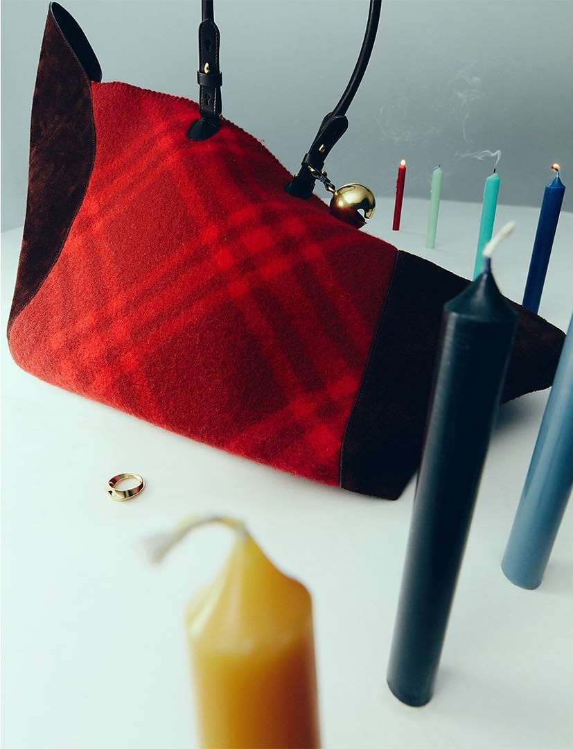 Red plaid wool purse with brown suede details and small gold ring sits next to lit candles in red, yellow, and shades of blue.