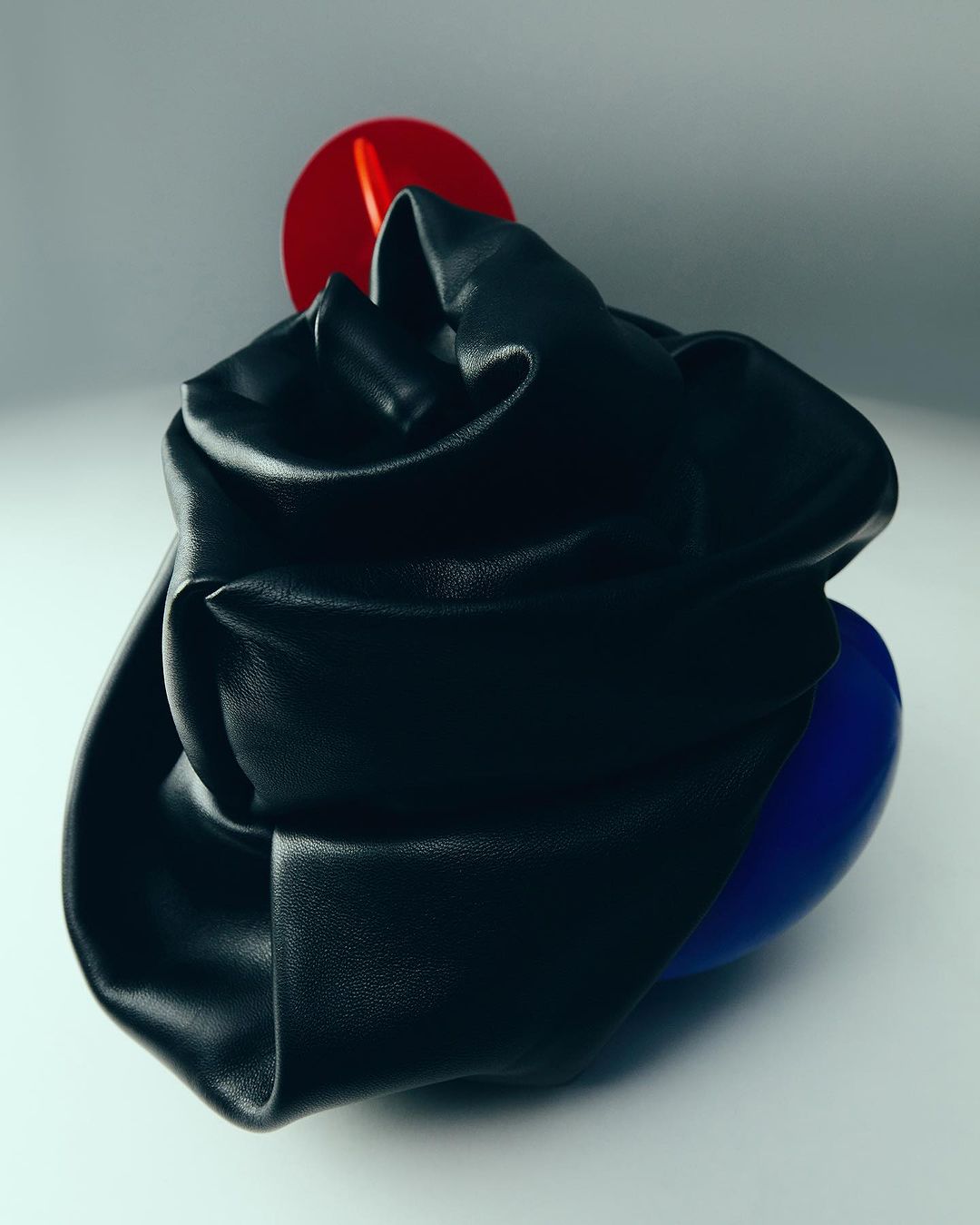 Abstract still life with crumpled black leather on geometric red and blue shapes set against a pale grey backdrop in a studio setting.