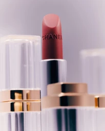 Close up of an open red lipstick tube with embossed lettering against a light grey studio background.