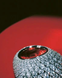Close-up of a paved diamond-set dome ring resting on a red surface under warm lighting.