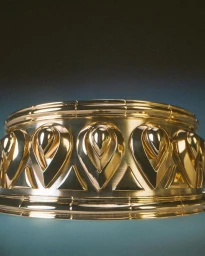 Close-up of a wide polished gold metal band with repeating teardrop and triangular embossed patterns