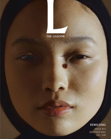 Close-up portrait of a woman wearing a black hood with a ladybug on her cheek, photographed by Anna Rosa Krau