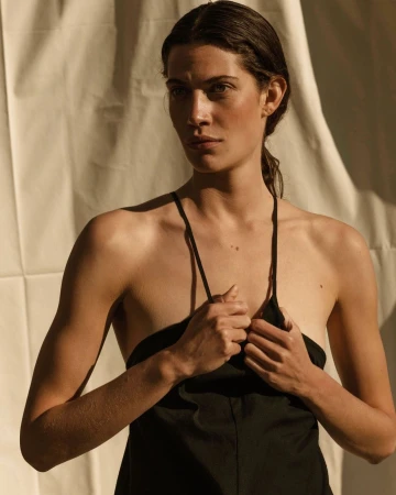 A woman in a black dress against a draped white fabric background in warm sunlight photographed by Anna Rosa Krau