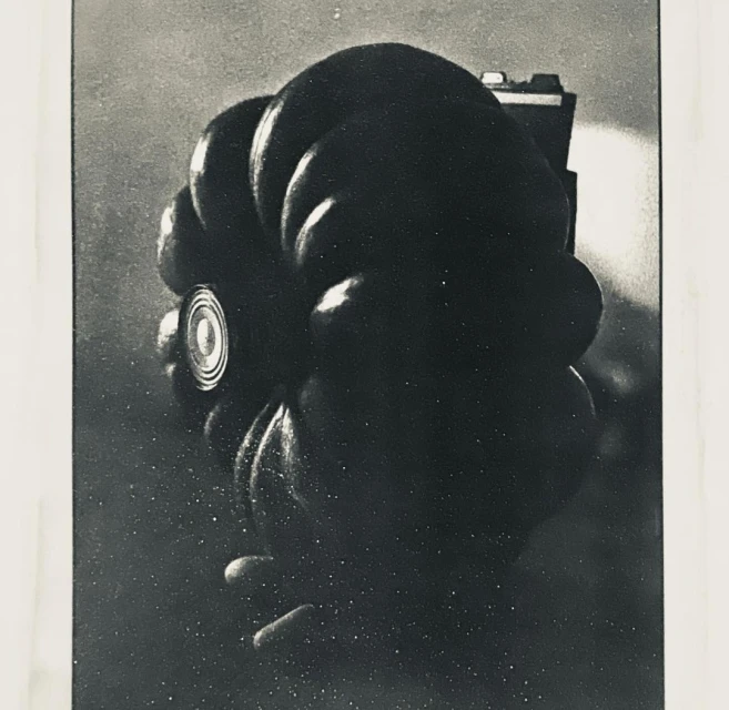 Close-up monochrome photograph of a Hasselblad camera with a Zeiss lens and a light source behind, set against a mottled backdrop.