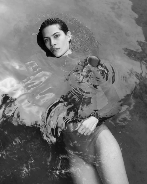 Black and white shot of a woman partially submerged in water, wearing a dark long-sleeved top, captured with natural light and soft reflections.