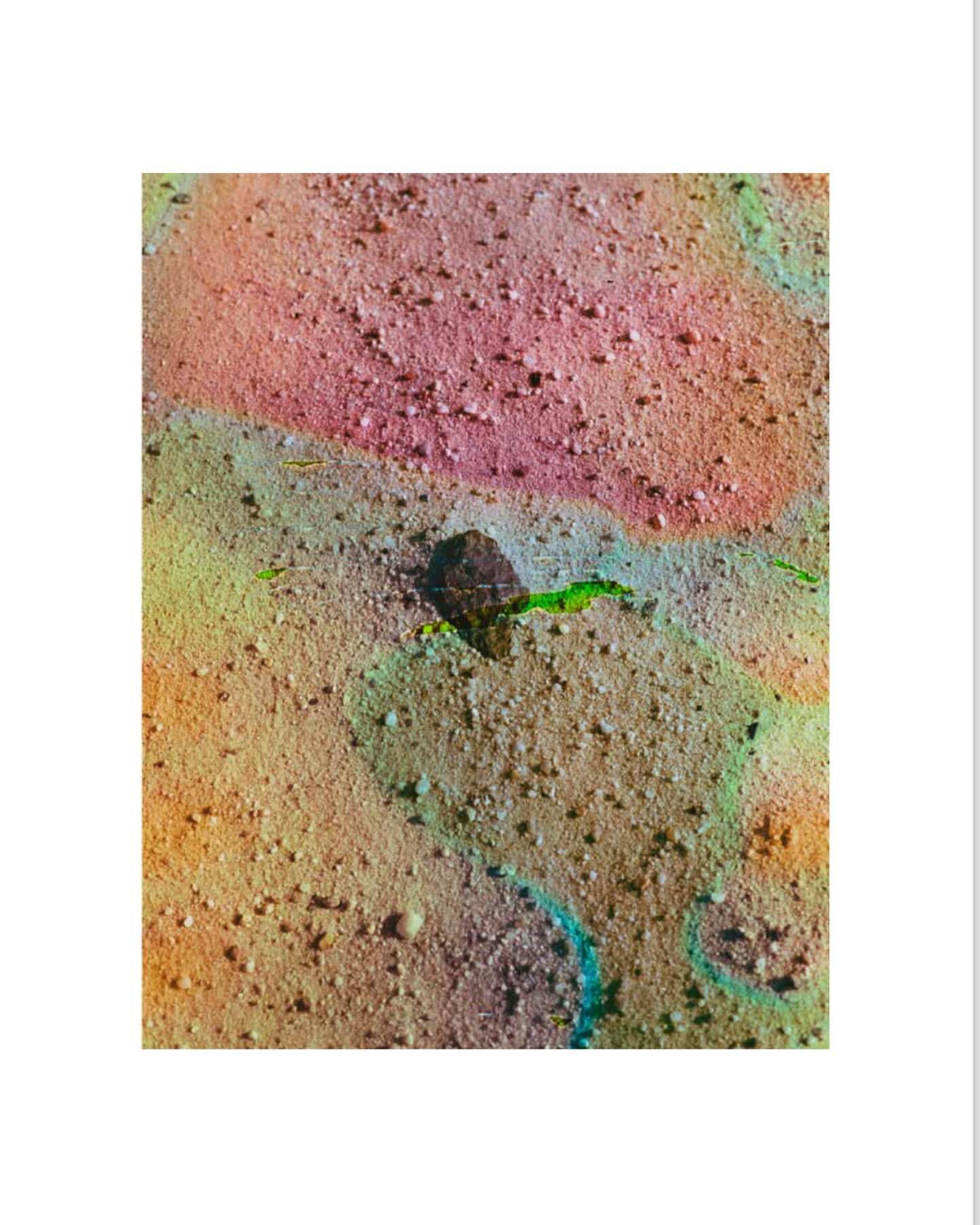 Close-up abstract image featuring rock fragment on a sandy surface with mottled colors of pink, yellow, brown, and turquoise.