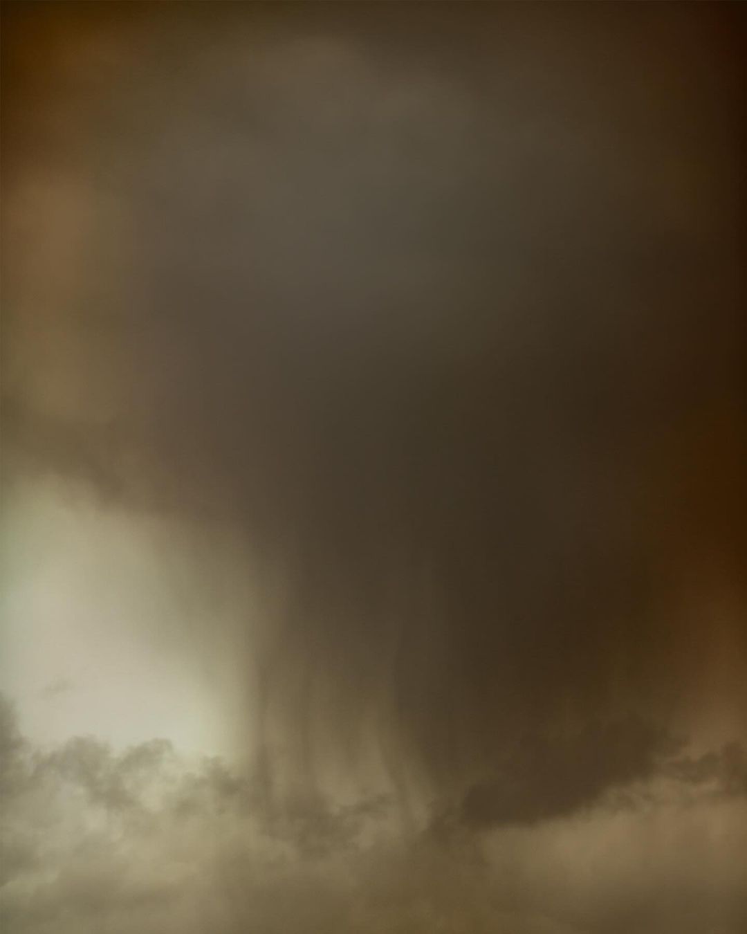 Dramatic cloudscape featuring dark, heavy storm clouds covering most of the frame with a patch of lighter clouds in the lower left corner.
