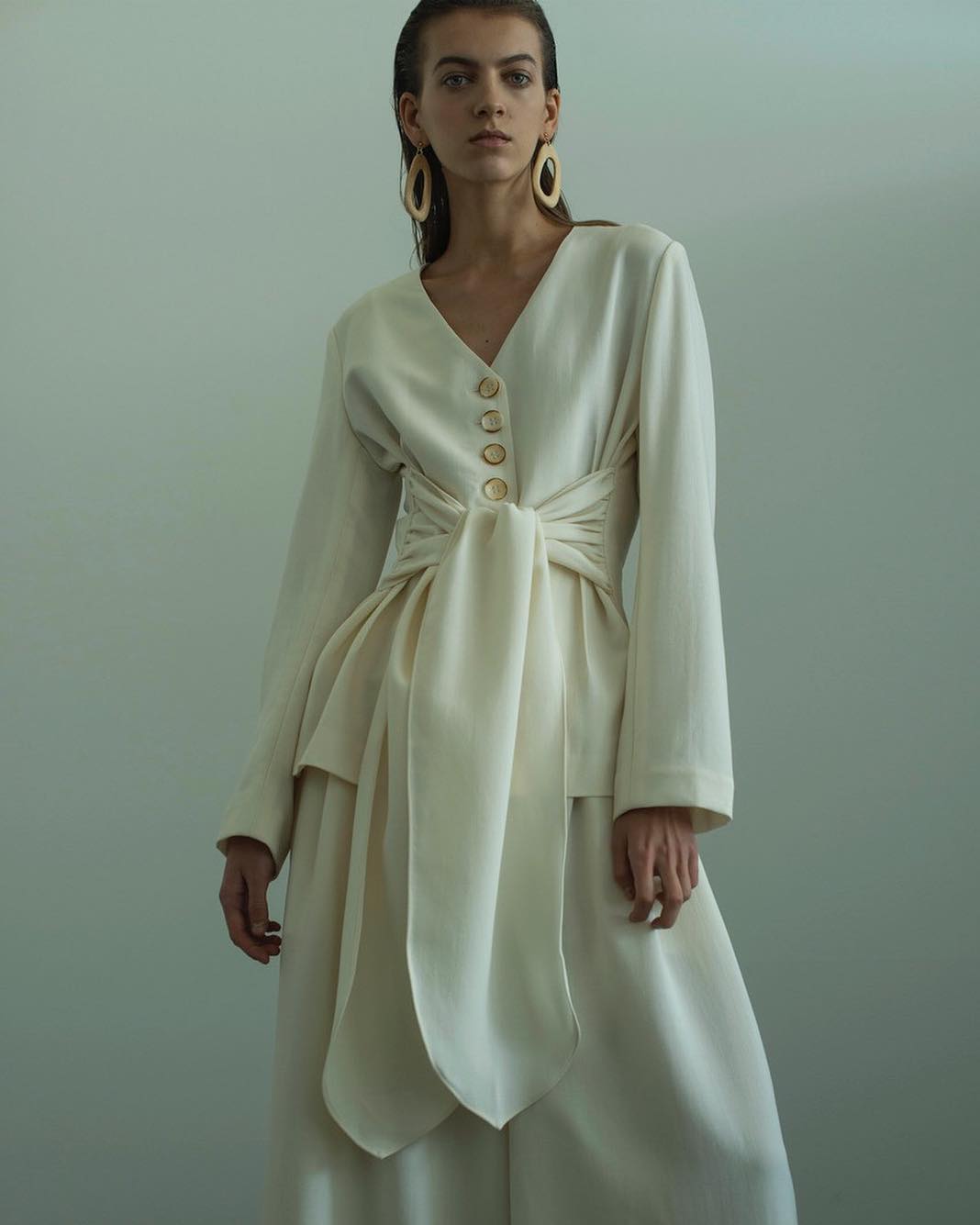 Woman wearing a cream-colored long-sleeved blouse with matching wide-leg trousers, posing against a neutral backdrop in a fashion setting.