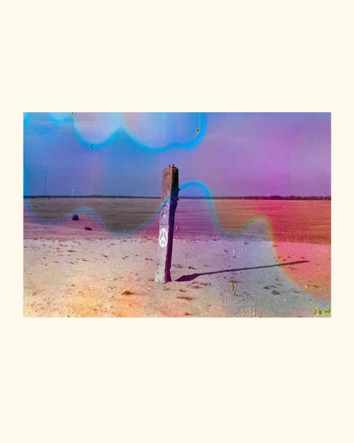 Weathered wooden post stands on a sandy landscape with a horizon view under a colorful sky, with an overlaid dreamy filter effect.