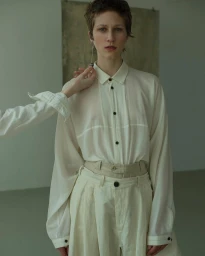 Model with short dark hair in a white button-down shirt and trousers, wearing a long drop earring.
