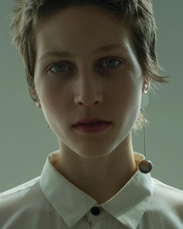 Close-up portrait of a young woman with short hair wearing a white collared shirt and a long drop earring.