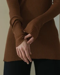 Close-up of a person wearing a ribbed brown knit sweater with fitted long sleeves, photographed by Anna Rosa Krau.