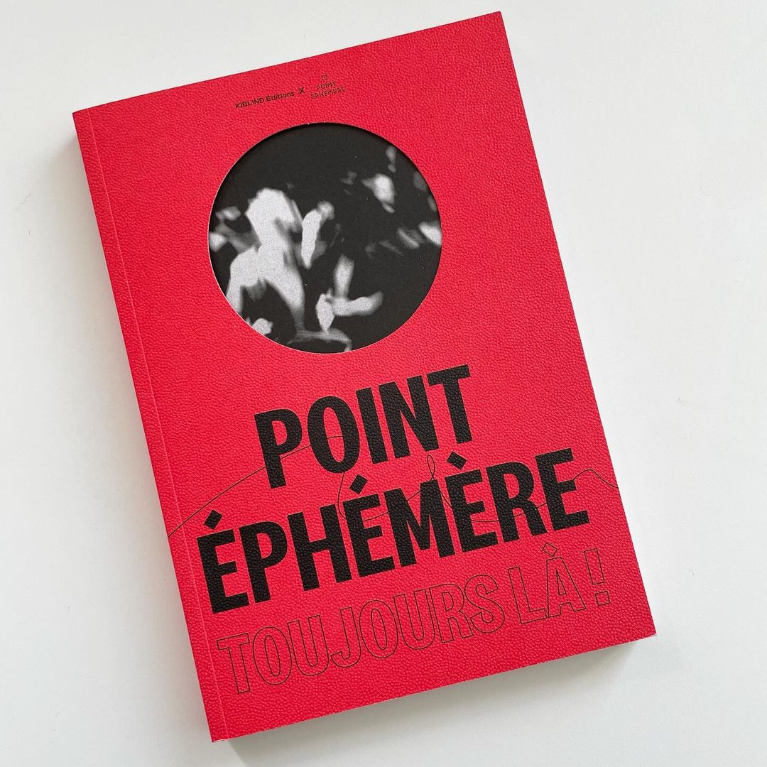 A red book titled 'Point Éphémère Toujours Là!' sits upright on a white surface, featuring a round cutout revealing an image.