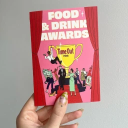 Hand holding a pink illustrated card for Food and Drink Awards with red curtains and a large trophy.