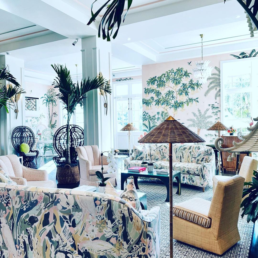 Living room interior with sofas and chairs featuring floral and leaf prints, indoor potted plants, and tropical-themed wall art.