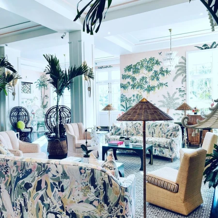 Living room interior with sofas and chairs featuring floral and leaf prints, indoor potted plants, and tropical-themed wall art.