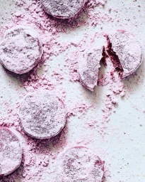 Overhead food photography of round purple pastries dusted in pink powder on a white textured surface.