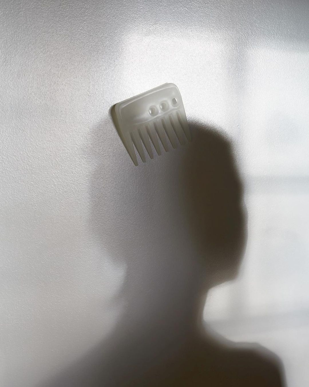 Silhouette of a person with a hair pick resting on their head, soft focus, diffused light against a solid background in a studio setting.