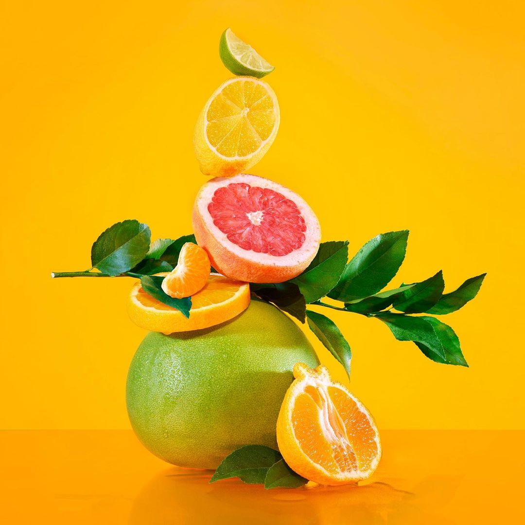 Still life photography of a vibrant citrus fruit arrangement featuring a pomelo base, stacked with orange, grapefruit, lemon, and lime slices.