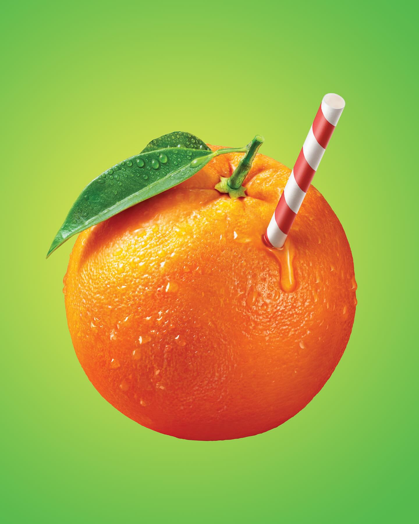An orange fruit with a green leaf and a striped straw, set against a gradient green background, highlights the vibrant colors.