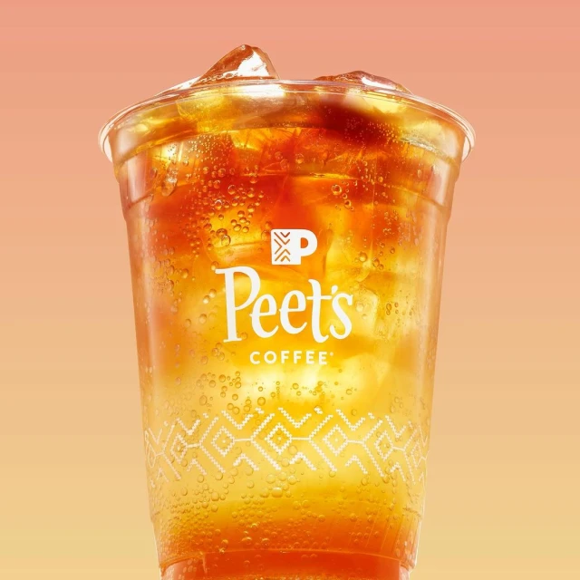 Iced coffee drink from Peet's Coffee in a clear plastic cup with logo and geometric design against an orange gradient background.