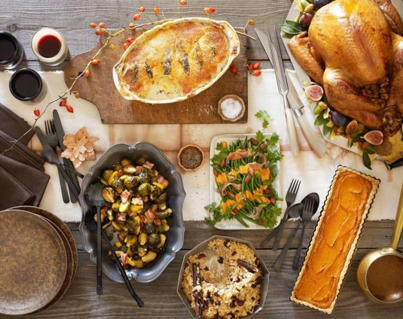 Overhead shot of a Thanksgiving table laden with roasted turkey, casseroles, salad, and pie, conveying a warm, autumnal feast.