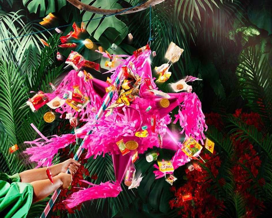 Festive piñata suspended amid lush tropical foliage and scattered candy, captured in a vibrant, eye-level studio shot.