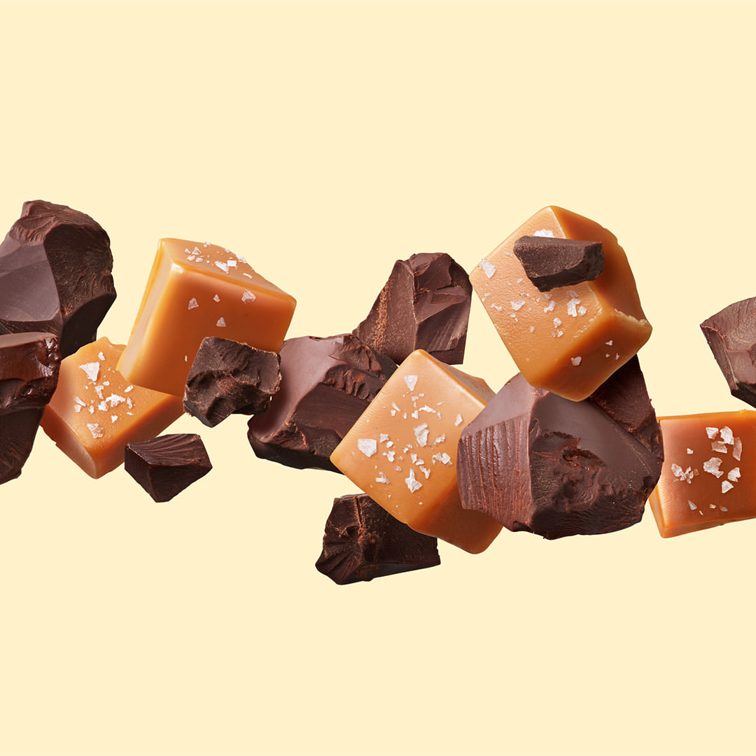 Chunks of dark chocolate and cubes of caramel with salt crystals float against a solid pale yellow backdrop. 