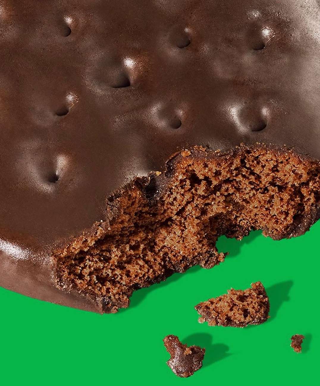 Close-up of a chocolate-covered cookie with a bite taken out on a vibrant green backdrop, highlighting textures and details.