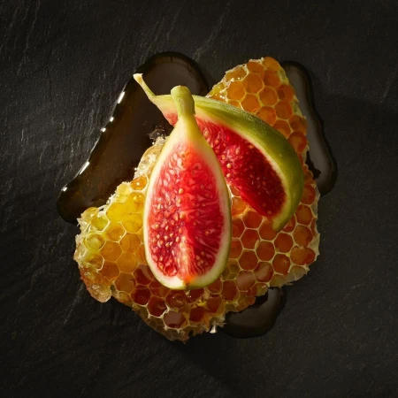 Overhead shot of sliced figs and honeycomb drizzled with honey on a dark surface, highlighting natural textures and rich colors.