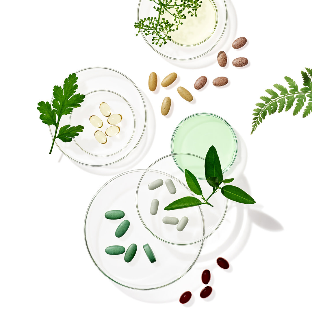 Overhead shot of transparent petri dishes filled with colorful vitamins and herbs on a clean, white background for healthcare concepts.