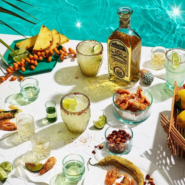 Table arrangement featuring a bottle of tequila, cocktails, shot glasses, and snacks, evoking a lively and refreshing atmosphere.