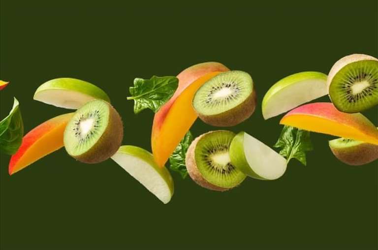 Green apples, sliced kiwis, spinach leaves, and cut mangos are horizontally arranged on a dark green background.