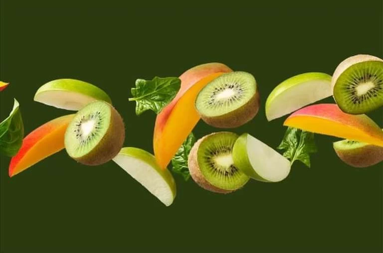 Green apples, sliced kiwis, spinach leaves, and cut mangos are horizontally arranged on a dark green background.