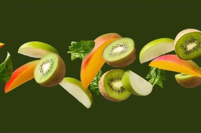Green apples, sliced kiwis, spinach leaves, and cut mangos are horizontally arranged on a dark green background.
