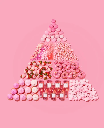 Overhead shot of pink desserts arranged in a triangle shape: macarons, candies, strawberries, doughnuts, cupcakes, mini wine bottles, marshmallows.