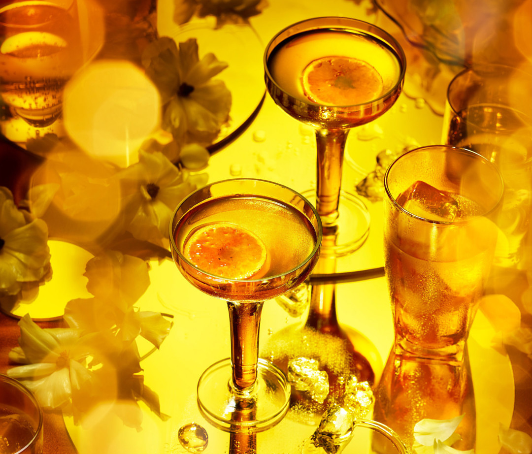 Golden-hued cocktail glasses with citrus slices, ice cubes, and flower accents creating an eye-catching and elegant beverage presentation.